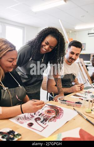 Smiling instructor assisting young woman in painting at desk in art class Stock Photo