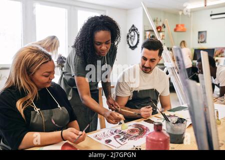 Mature female instructor teaching painting to young students at desk in art class Stock Photo