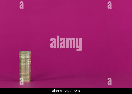 UK British Pound Sterling GBP single gold coloured coin stack, image left on a vibrant purple background with copy space