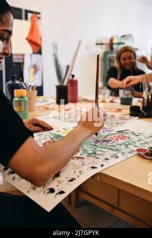 Female painter painting on paper at table in art class Stock Photo