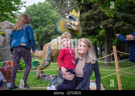 Mother holding her son in her arms and having fun in the dinosaurs festival. Stock Photo
