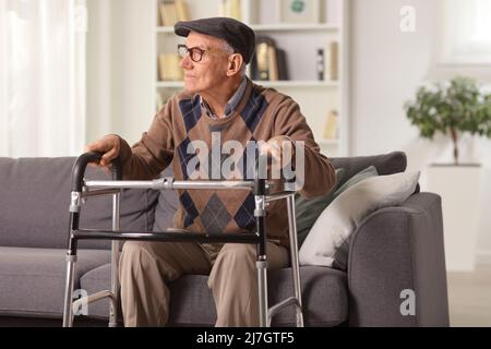 Elderly man sitting on a sofa and holding onto a walker Stock Photo