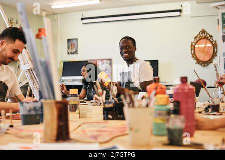 Portrait of happy young man holding paint container in art class Stock Photo