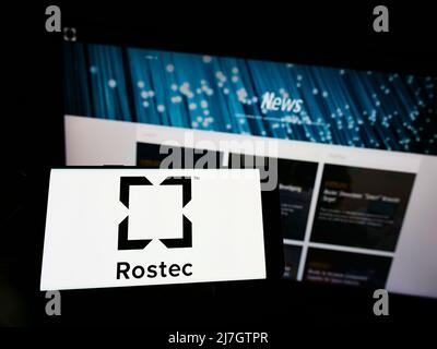 Person holding mobile phone with logo of Russian defense company Rostec on screen in front of business web page. Focus on phone display. Stock Photo
