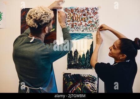 Smiling female and male students sticking painting on wall in art class Stock Photo