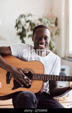 Portrait of happy young man practicing guitar while sitting in classroom Stock Photo