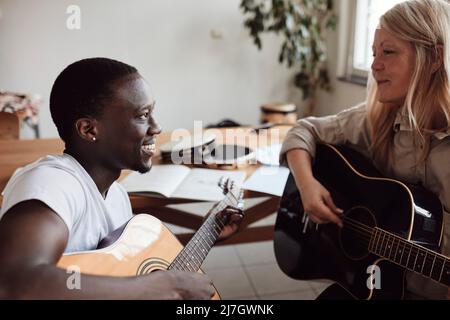 Smiling female mature tutor teaching guitar to young man in classroom Stock Photo