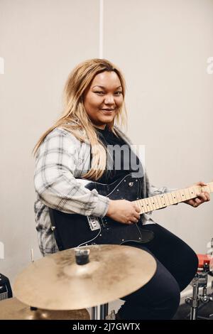 Portrait of smiling young woman practicing guitar in classroom Stock Photo