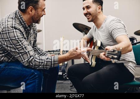 Happy man practicing guitar sitting with friend in classroom Stock Photo