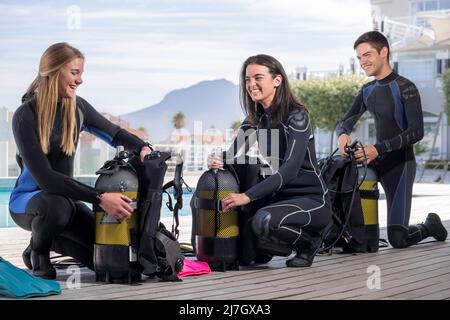A group of scuba divers kitting up their dive gear on a deck next to a pool Stock Photo