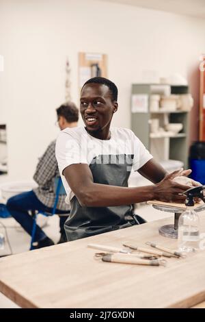 Young man wearing apron molding clay while sitting at table in classroom Stock Photo