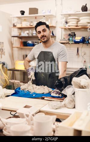 Young man wearing apron standing with clay at table in art class Stock Photo