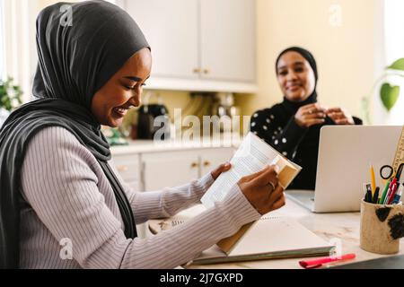 Smiling young woman reading book while sitting with female friend at table Stock Photo