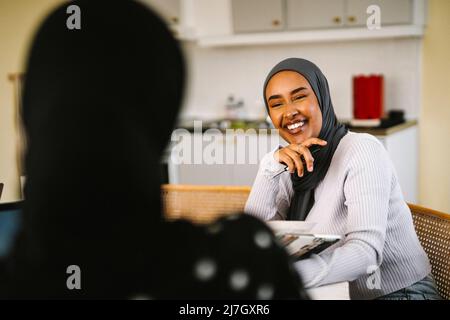 Happy young woman wearing hijab talking with friend at home Stock Photo