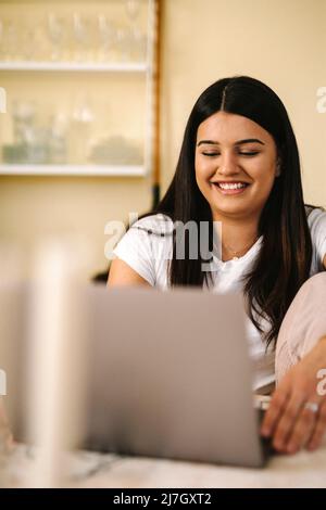Happy young female freelancer using laptop sitting at table Stock Photo