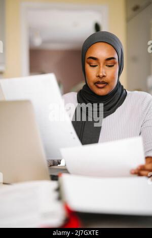 Young female freelancer analyzing documents while working from home Stock Photo