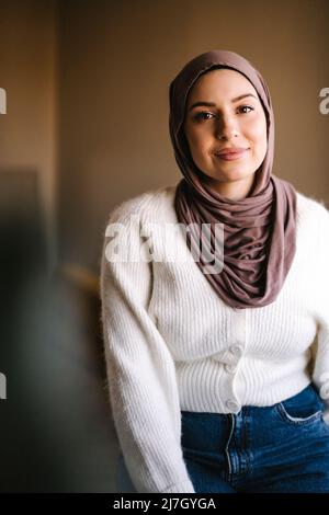 Portrait of smiling young woman wearing hijab at home Stock Photo