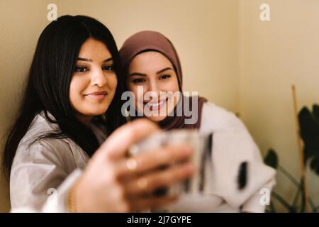Young woman taking selfie with friend through smart phone at home Stock Photo
