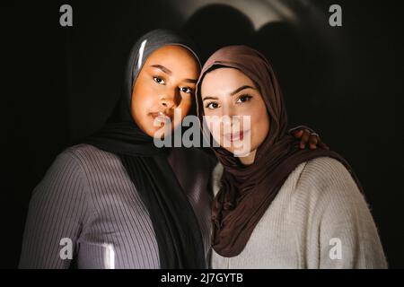 Young women wearing hijabs standing against gray background Stock Photo