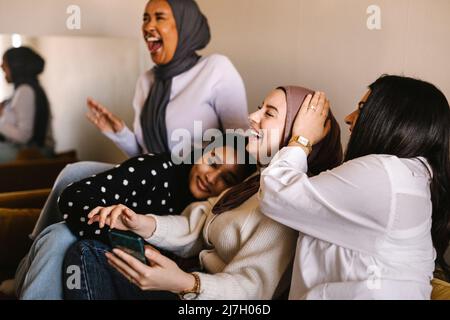 Young women laughing while sitting together on sofa at home Stock Photo