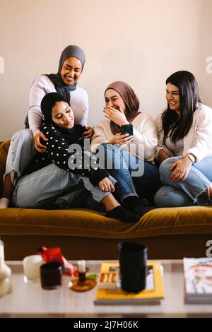 Happy young women laughing while sitting together on sofa enjoying at home Stock Photo