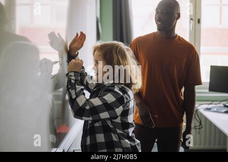 Student solving maths sum on whiteboard while standing by male teacher in classroom Stock Photo