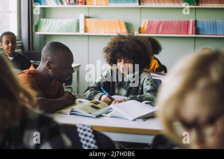 Male teacher assisting boy studying at desk in classroom Stock Photo