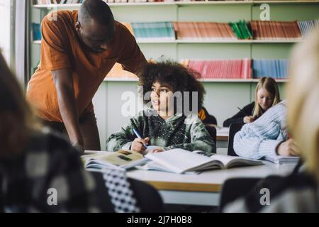 Male teacher helping student while studying in classroom Stock Photo