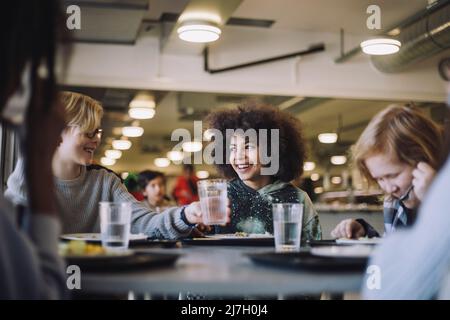 Boy passing drinking glass to friend during lunch break at school Stock Photo