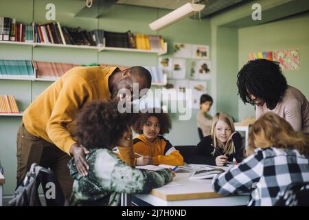 Teachers assisting students while studying in classroom at school Stock Photo