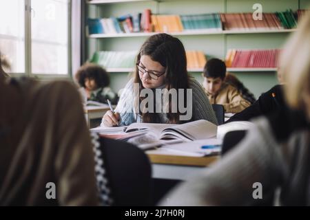 Girl writing while sitting at desk during exam in classroom Stock Photo