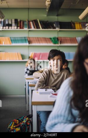 Schoolboy sitting on desk in classroom Stock Photo