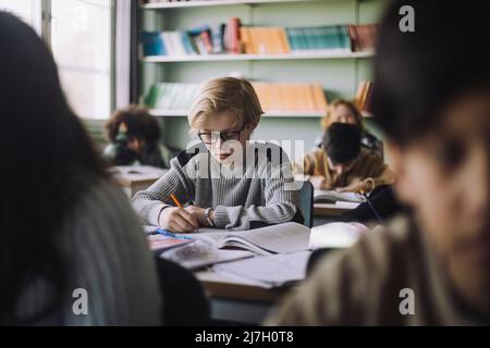 Pupil writing in book during exam in classroom Stock Photo