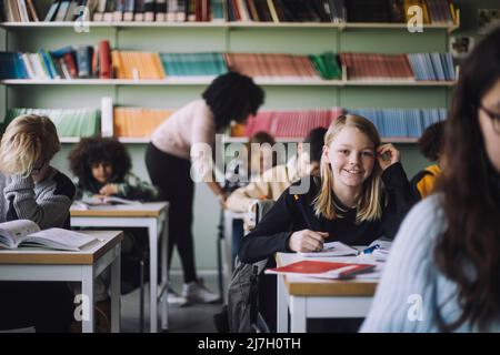 Portrait of smiling student sitting at desk in classroom Stock Photo