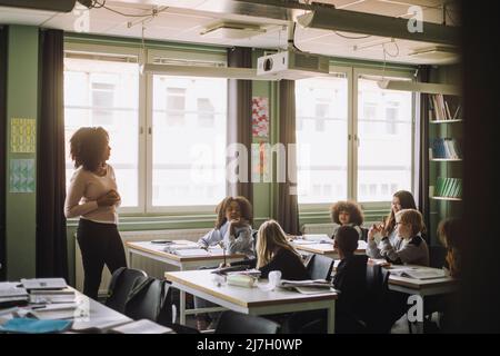 Students and teacher discussing during lecture in classroom Stock Photo