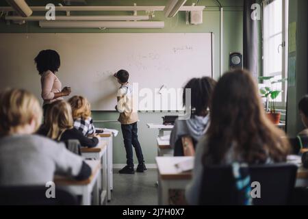 Student solving maths sum on white board in classroom Stock Photo