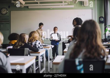 Boys holding reports while doing presentation to students in classroom Stock Photo