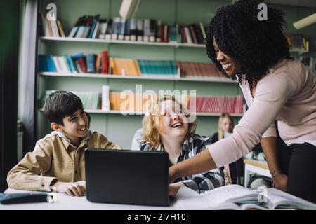 Smiling teacher helping students while doing e-learning in classroom Stock Photo