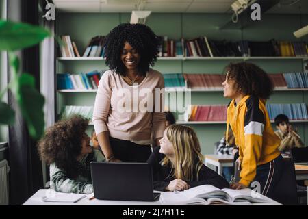 Smiling teacher interacting with students while doing e-learning in classroom Stock Photo