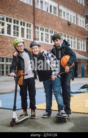 Boy holding push scooter with friends standing on skateboard in front of school building Stock Photo