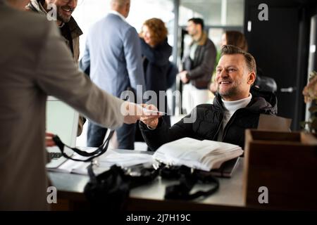 Smiling disabled businessman taking ID card from receptionist at registering counter Stock Photo