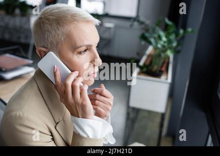 thoughtful businesswoman calling on mobile phone in blurred office Stock Photo