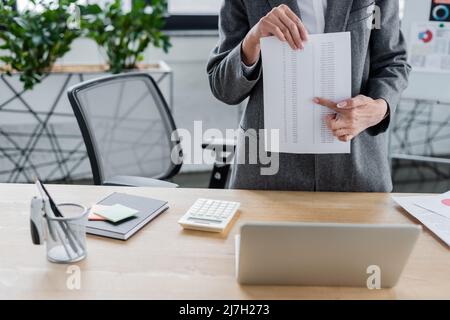 cropped view of economist pointing at document during online conference on blurred flip chart Stock Photo