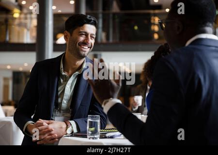 Happy businessman leaning on table while talking with entrepreneur at seminar Stock Photo