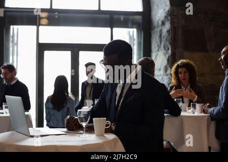 Businessman with laptop on table writing in notepad while standing at seminar Stock Photo