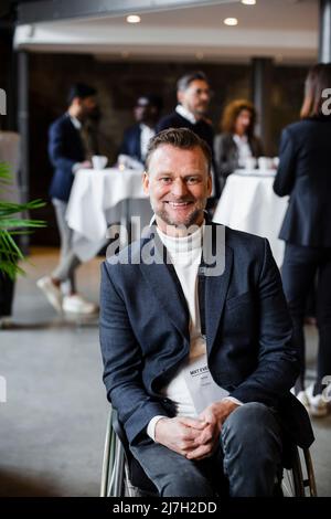 Portrait of smiling disabled businessman sitting in wheelchair at seminar Stock Photo