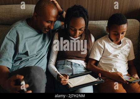 Father sitting with daughter and son using wireless technologies at home Stock Photo
