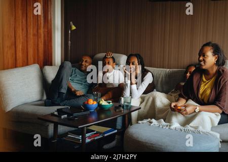 Family watching TV together while sitting on sofa at home Stock Photo