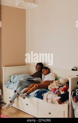 Siblings reading story book together while sitting on bed at home Stock Photo