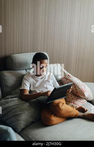 Boy using tablet PC while sitting on sofa at home Stock Photo